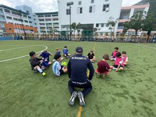 Little Dragons sitting with their coach on the pitch